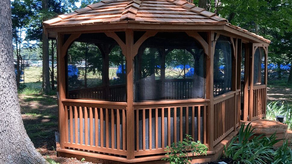 Gazebo corner with cedar-shingle roof | Tycos Roofing And Siding Inc Corner perspective of a wooden gazebo showing railings and a cedar-shingle roof.