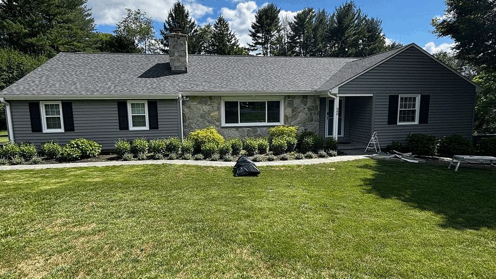 Ranch house with new gray shingle roof and stone siding under blue sky