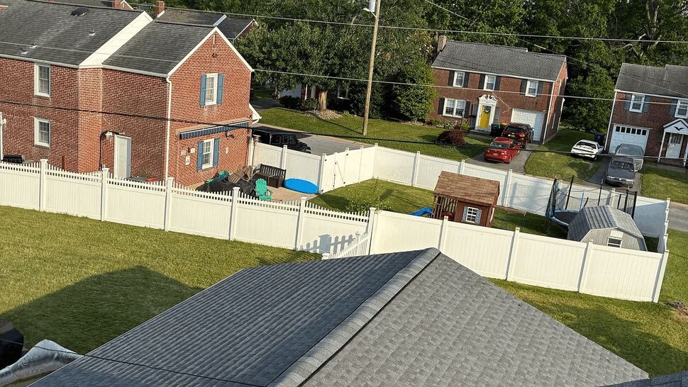 Aerial view of gray shingle roofs, garages and fenced backyards in a neighborhood.