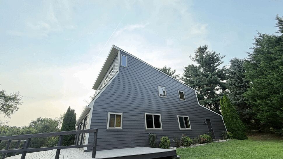 Exterior Siding on Modern Home | Tycos Roofing And Siding Inc Side view of a gray house showing horizontal siding, deck railing, and windows.