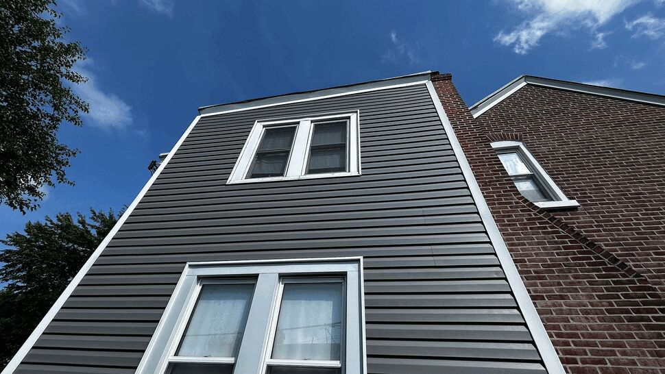 Two-story gray vinyl siding with white framed windows against blue sky