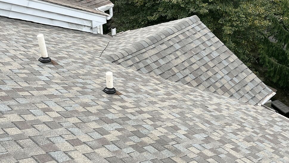 Close-up of grey asphalt shingle roof with two plumbing vents and surrounding gutters.