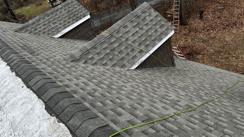 Top-down view of a grey asphalt shingle roof with a safety rope stretched across it.