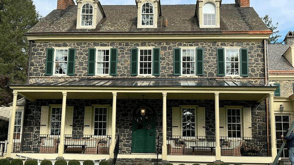 Stone colonial home with dormered roof, green shutters and wide front porch