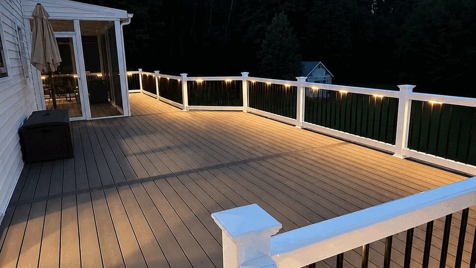 Illuminated composite deck at dusk | Tycos Roofing And Siding Inc Close-up of deck boards and railing lights at dusk