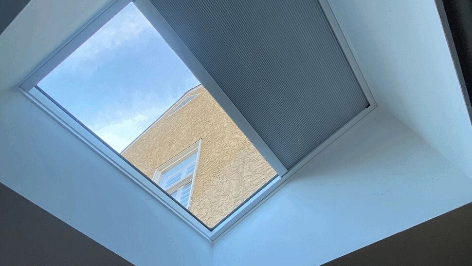 Interior view looking up at a skylight with a half-open pleated blind.