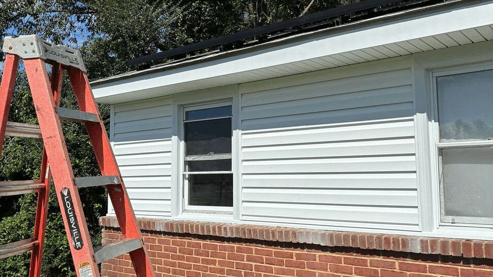 Ladder at eaves for gutter work | Tycos Roofing And Siding Inc Orange ladder leaning against house eaves and siding during exterior work