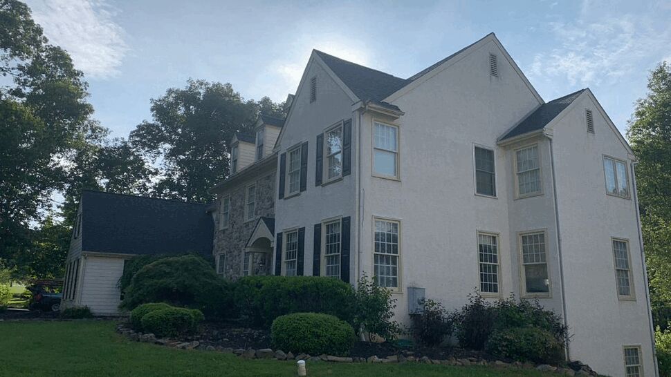 Wide view of colonial-style two-story home with shingled roof and landscaped front yard.