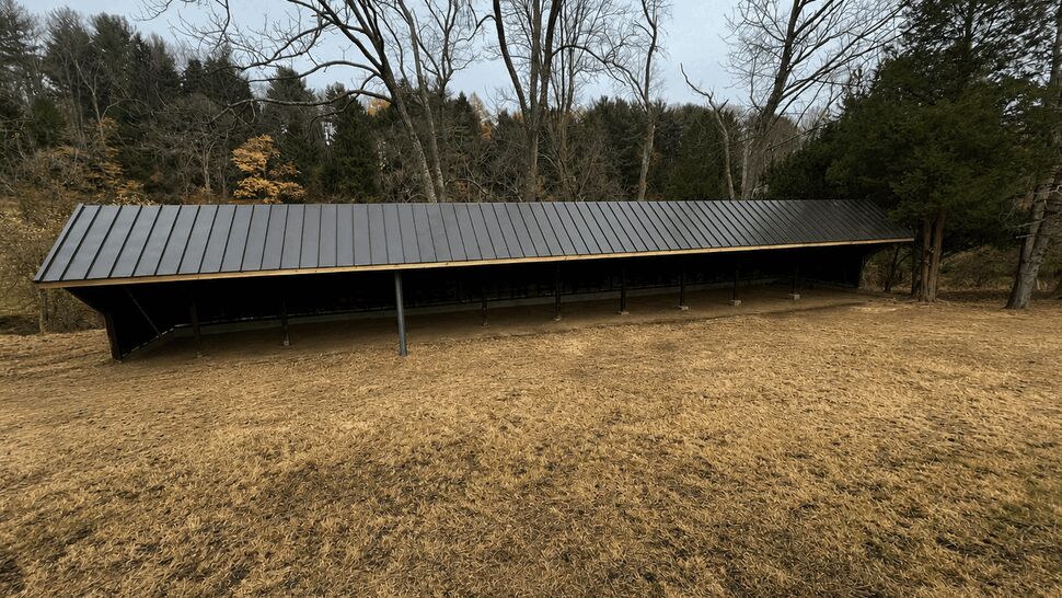 Long dark metal standing-seam lean-to roof over open storage area.