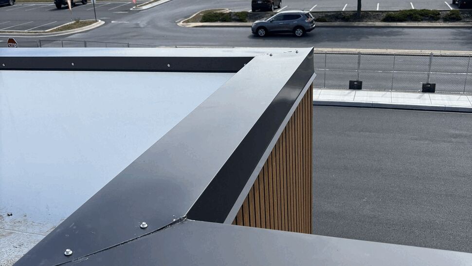 Close-up of metal roof edge coping and fasteners overlooking a parking area