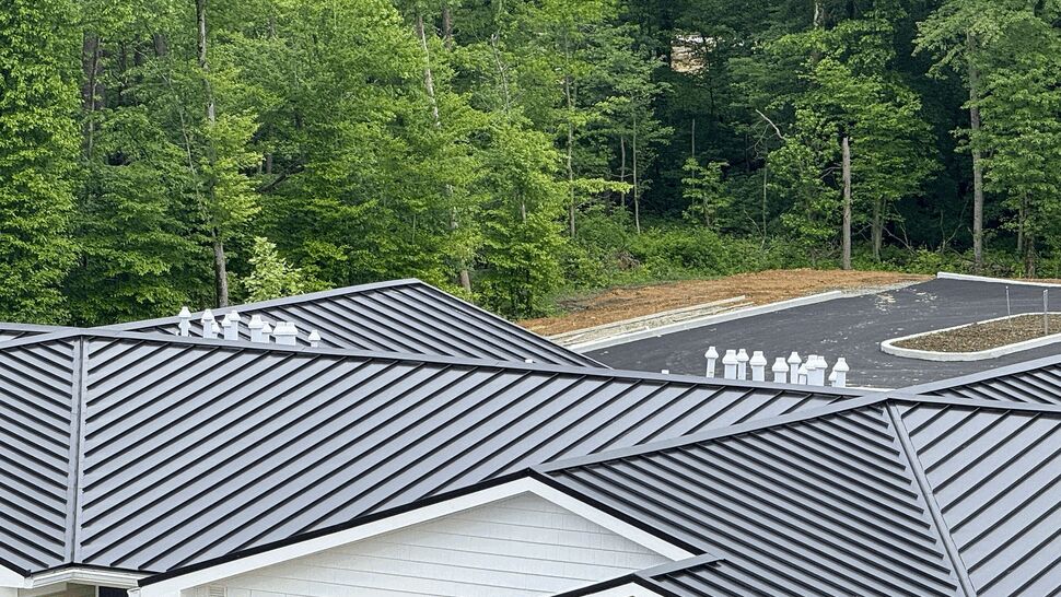 Diagonal view of dark metal roof with multiple vent stacks and surrounding trees