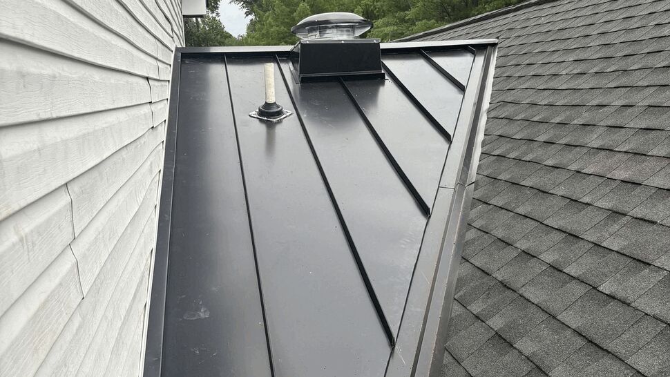 Triangular metal roof valley between house walls with roof vent pipe