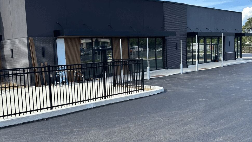 Black commercial storefront with large glass windows and asphalt parking lot