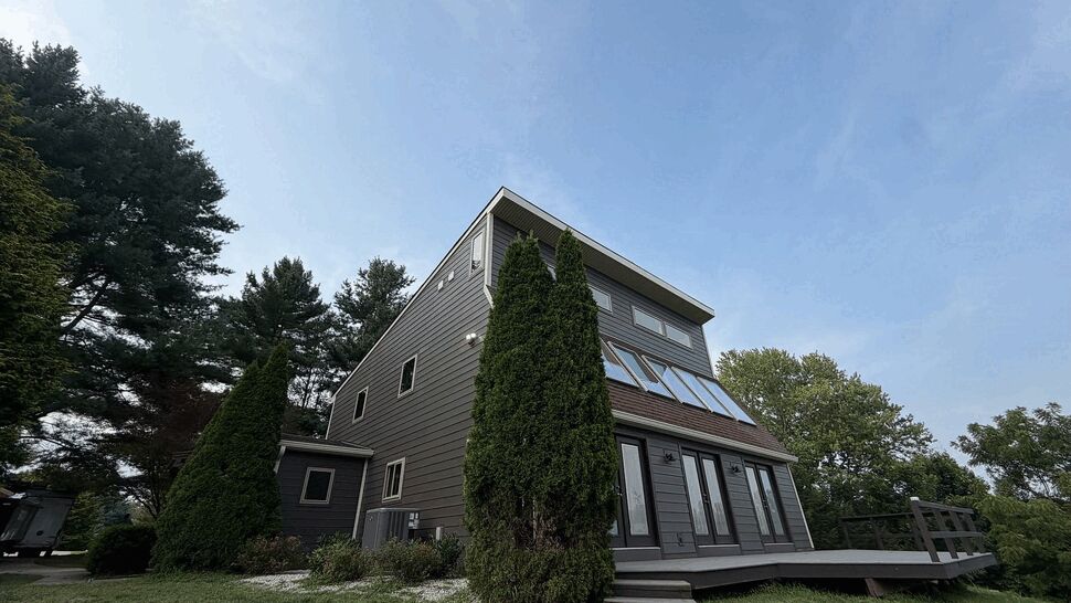 Raised Deck and Exterior Trim | Tycos Roofing And Siding Inc Two-story gray home with a raised wooden deck and tall evergreen trees.