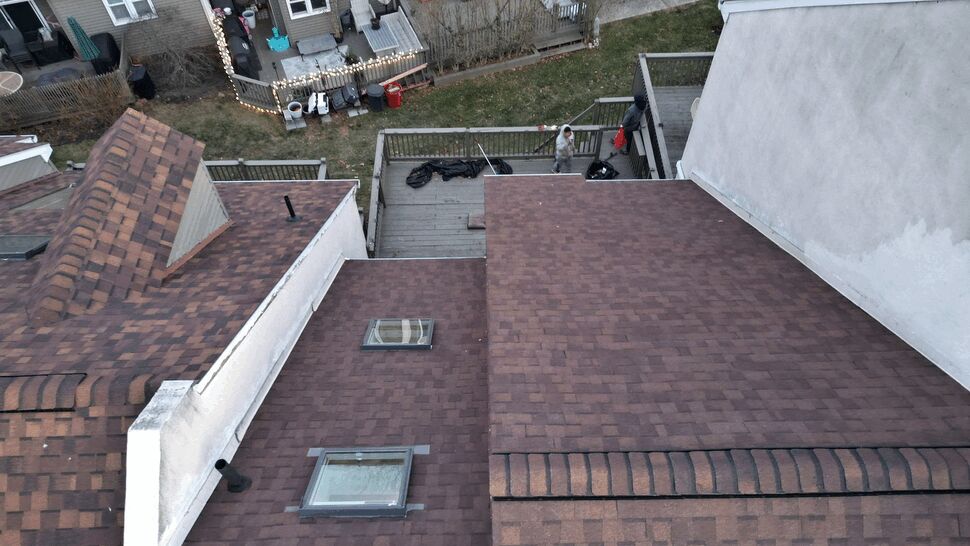 Overhead view of multi-level brown shingle roofs with skylights and backyard deck