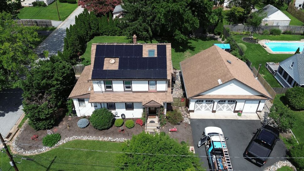 Aerial view of a home with dark solar panels on the roof and detached garage