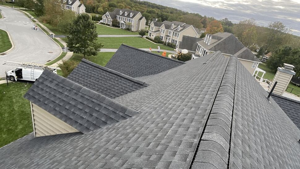 Perspective down a long roofline with neighboring homes and cloudy sky in the background.