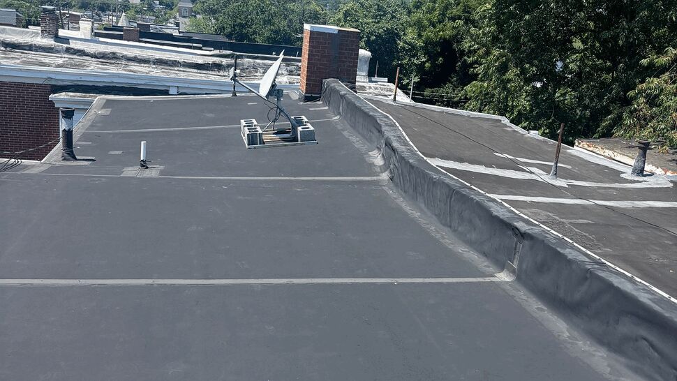 Smooth black flat roof membrane with vents and a satellite on a sunny day.