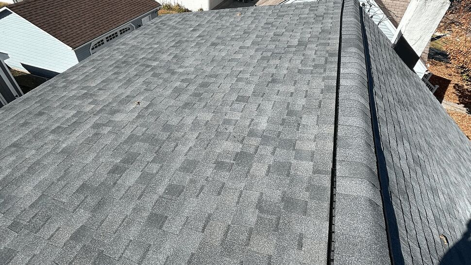 Aerial view of a gray asphalt shingle roof with a ridge vent and neighboring houses.