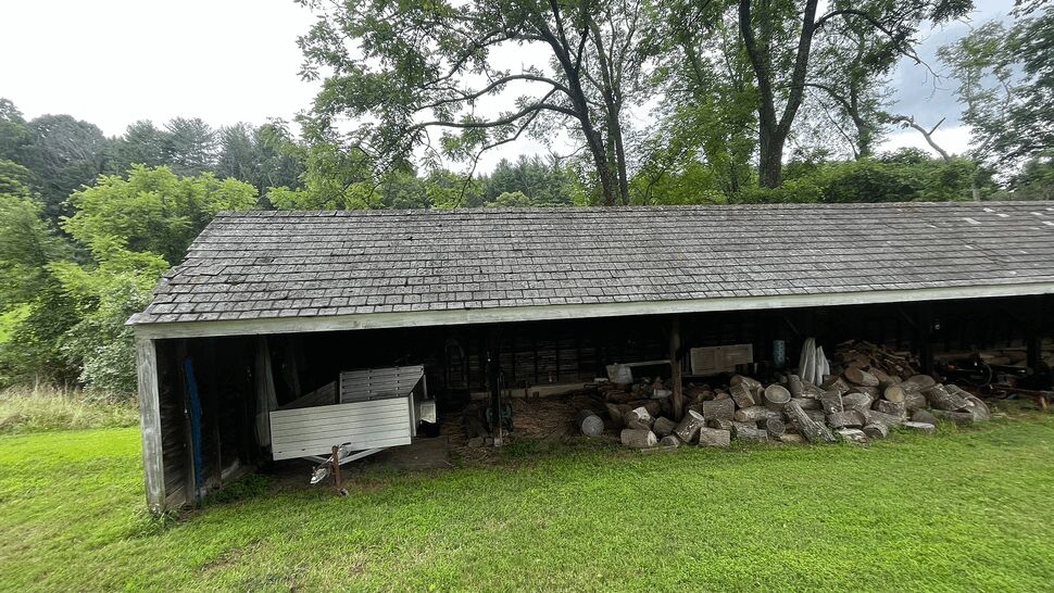 Open storage shed with aged wood siding and stacked firewood under roof.