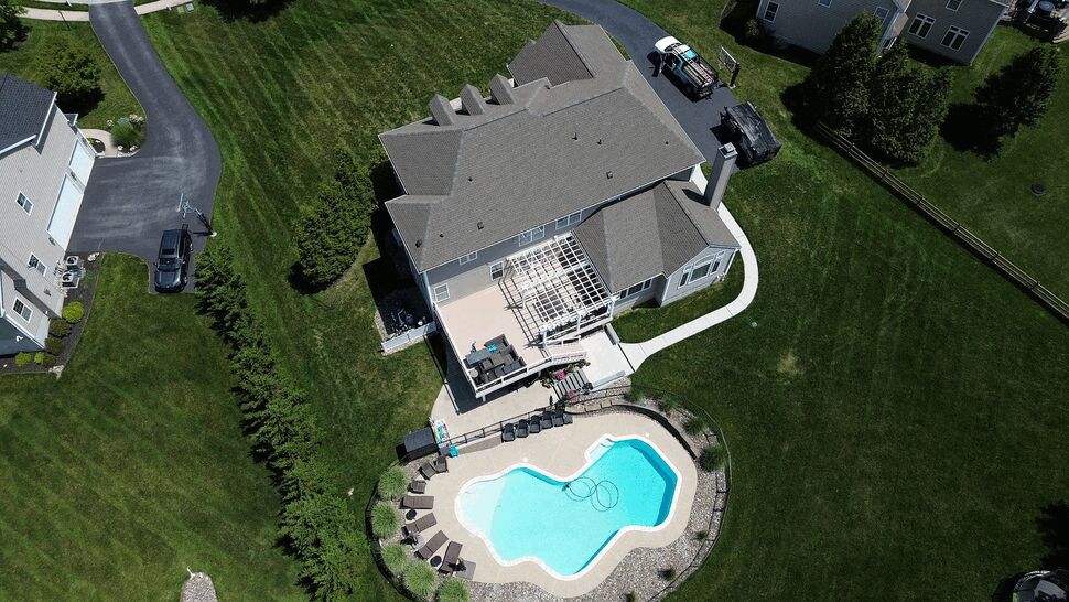 Top-down view of backyard deck, pergola and pool behind a home