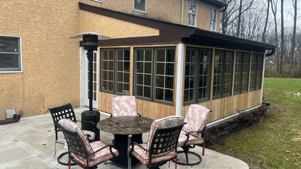 Back patio with table and chairs beside an enclosed glass sunroom.
