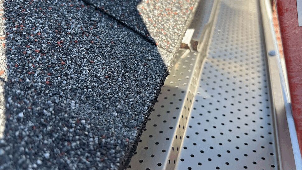 Perforated Gutter Guard Installation | Tycos Roofing And Siding Inc Close-up of perforated metal gutter guard next to asphalt shingles
