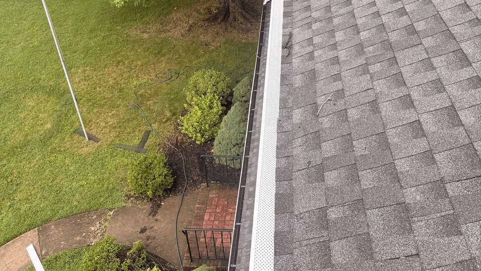 Perforated gutter guard on shingle roof | Tycos Roofing And Siding Inc Perforated gutter guard along grey shingle roof edge viewed from above