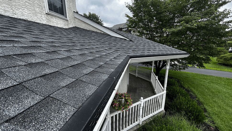 Close-up of porch roof edge with gutter guard, white railing, and gray shingles