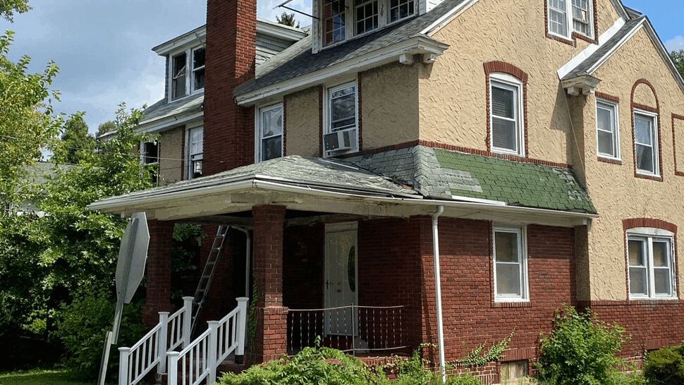 Porch roof showing worn and missing shingles with a ladder against the house.