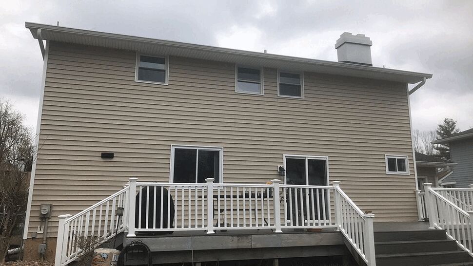 Rear view showing white-railed deck, sliding glass doors and beige vinyl siding.