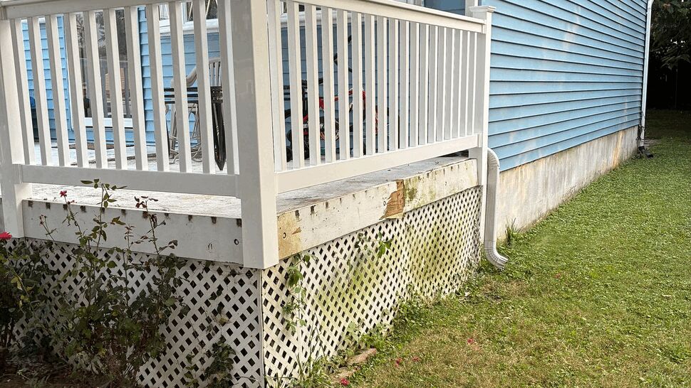 Deck lattice skirting with white gutter downspout beside blue siding