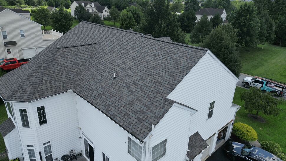 Backside aerial of home's shingled roof above a deck and garage area.