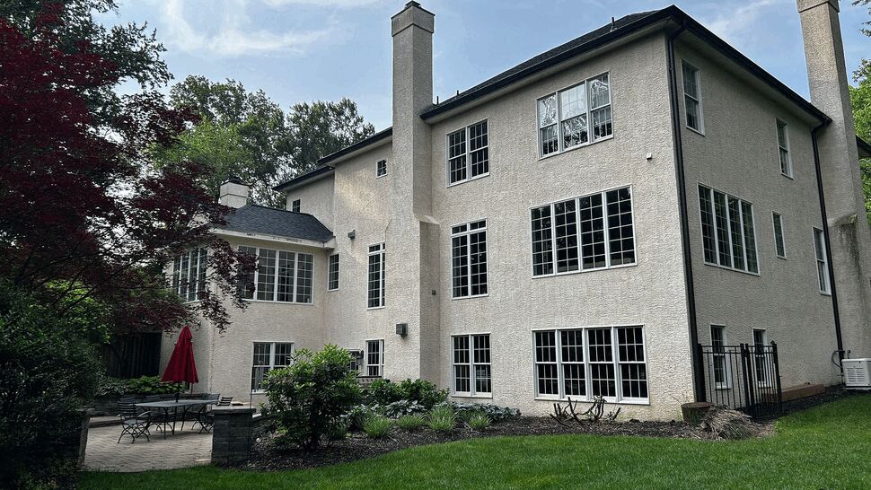Rear view of stucco house with many large windows and patio area