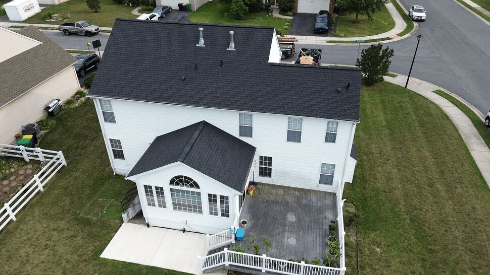 Back of house with sunroom, deck and dark roof from an aerial angle.