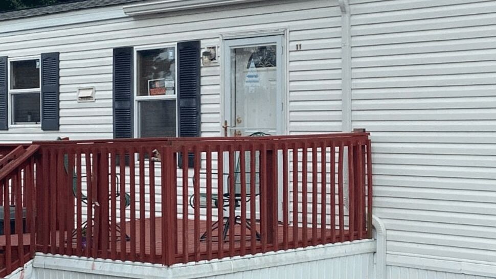 Red wooden deck attached to a white mobile home with vinyl siding and downspout.