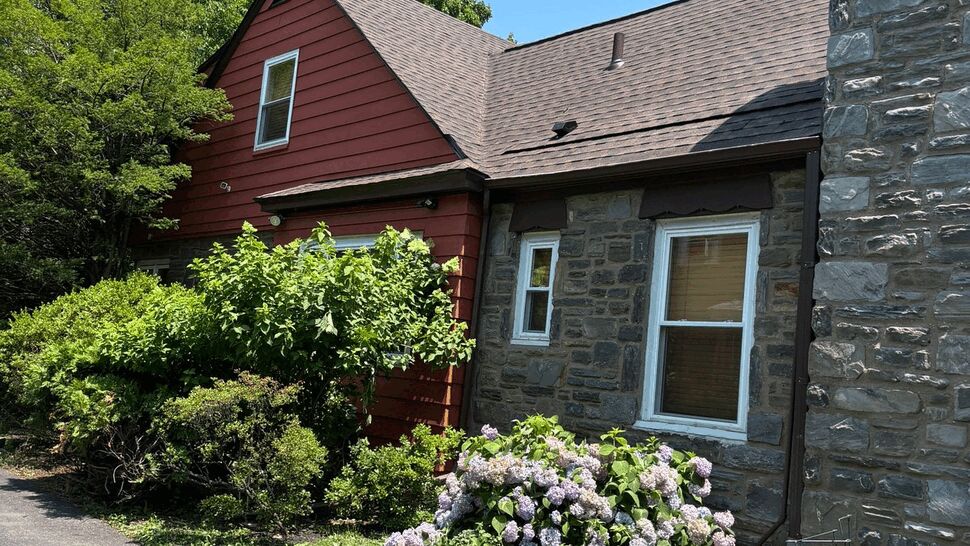 Red sided and stone exterior home with hydrangeas and driveway.