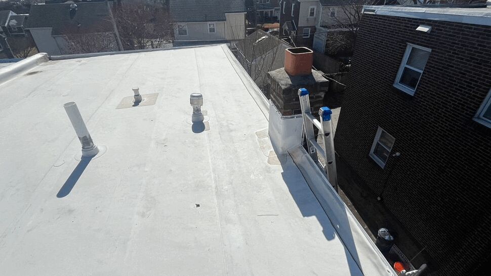 White flat roof with chimney, vents and neighboring houses in background.