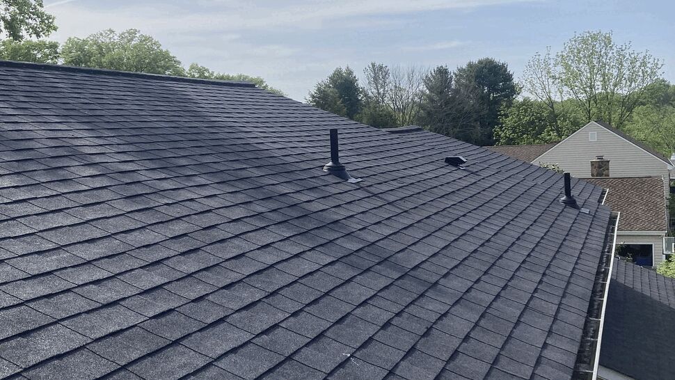Wide view of residential shingle roof with vents and gutter under blue sky