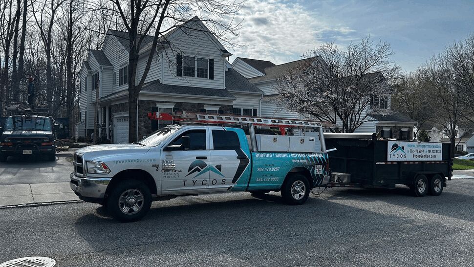 Tycos pickup truck and debris trailer staged in front of a suburban house for a roofing job.