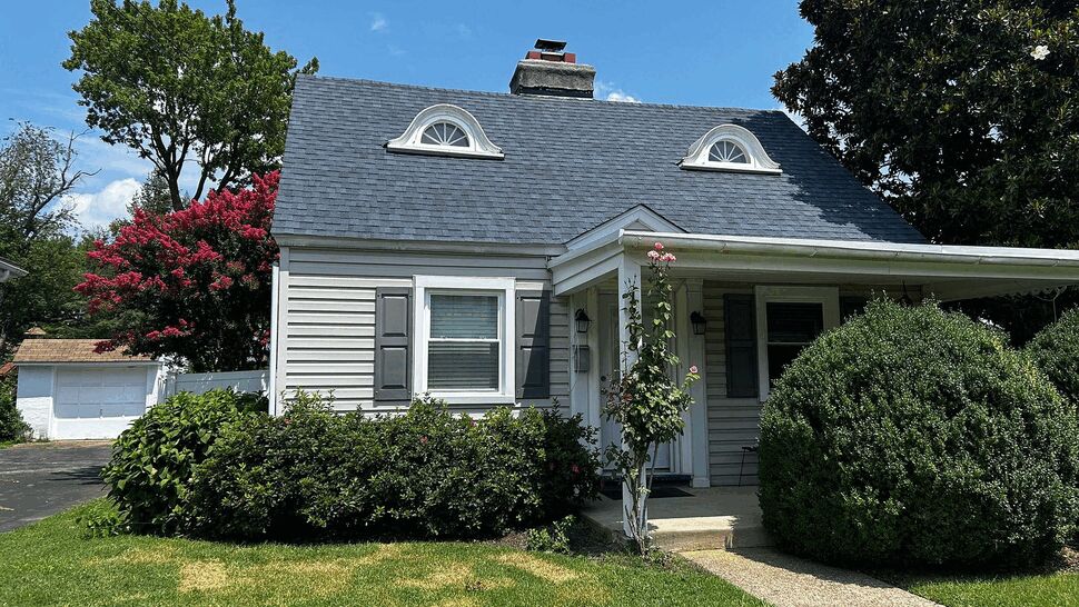 Front porch and gray shingle roof with shrubs and walkway leading to entrance.