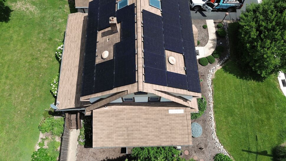 Bird's-eye view of roof ridge with solar panels and white exterior siding