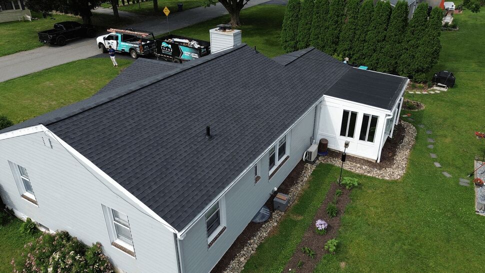 Angled aerial of house roof with attached four season room and surrounding landscaping.