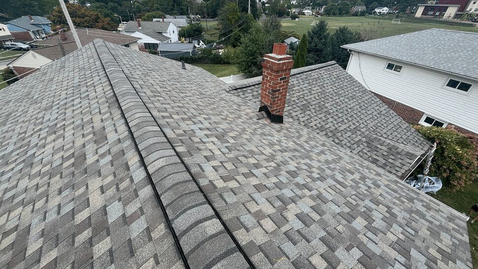 High rooftop view showing chimney flashing, ridge cap, and grey shingles.