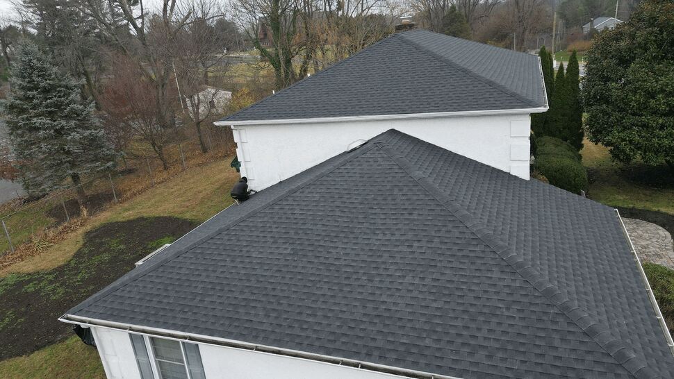 Close aerial of roof corner showing shingles, fascia, and attached gutters.
