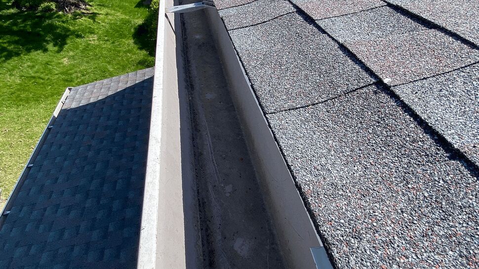 Roof Edge and Gutter Channel | Tycos Roofing And Siding Inc Close-up of a roof edge and open gutter channel beside a tree-lined yard.