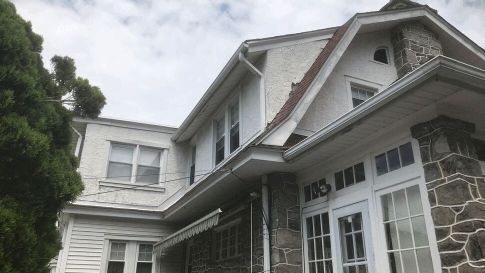 Close-up of roof eave and white gutter above stone exterior