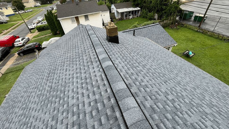 Roof Ridge and Chimney | Tycos Roofing And Siding Inc Aerial view of gray shingle roofing with ridge caps and a chimney.