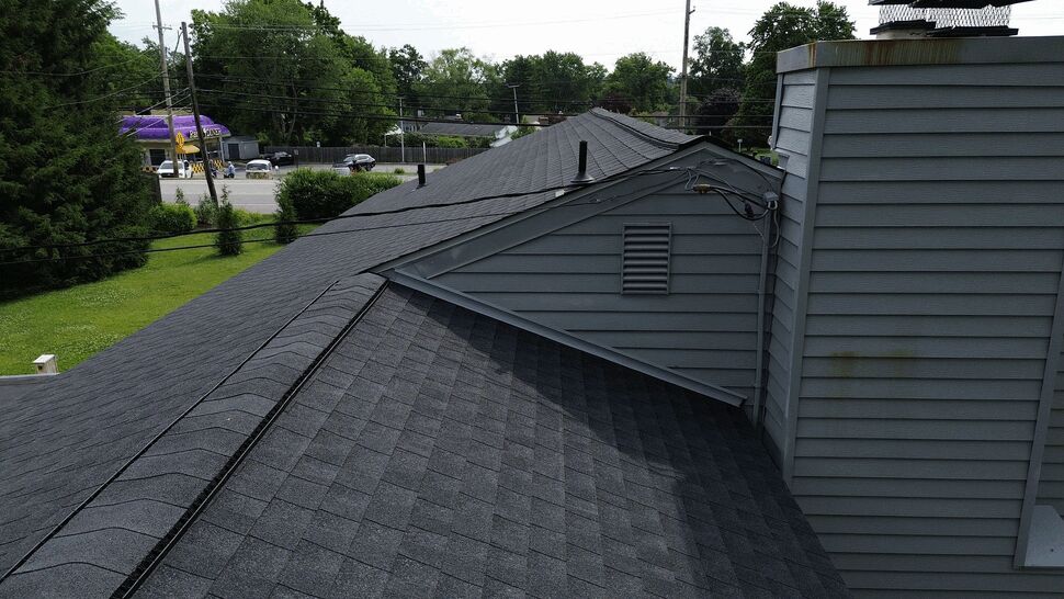 Close-up view of roof ridge, chimney base, vents, and asphalt shingles.