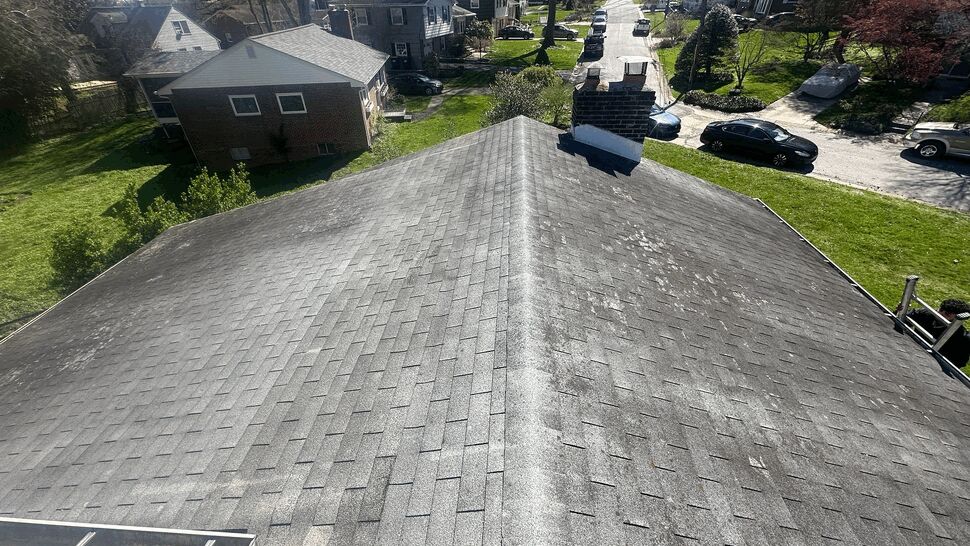 Aerial view of shingled roof ridge and chimney overlooking the neighborhood